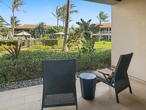A patio with two chairs and a small table, overlooking a well-maintained garden with palm trees and a golf course in the background. - Spacious Ground-Level Villa Near Pool, Beachfront Resort Amenities (Lahaina)