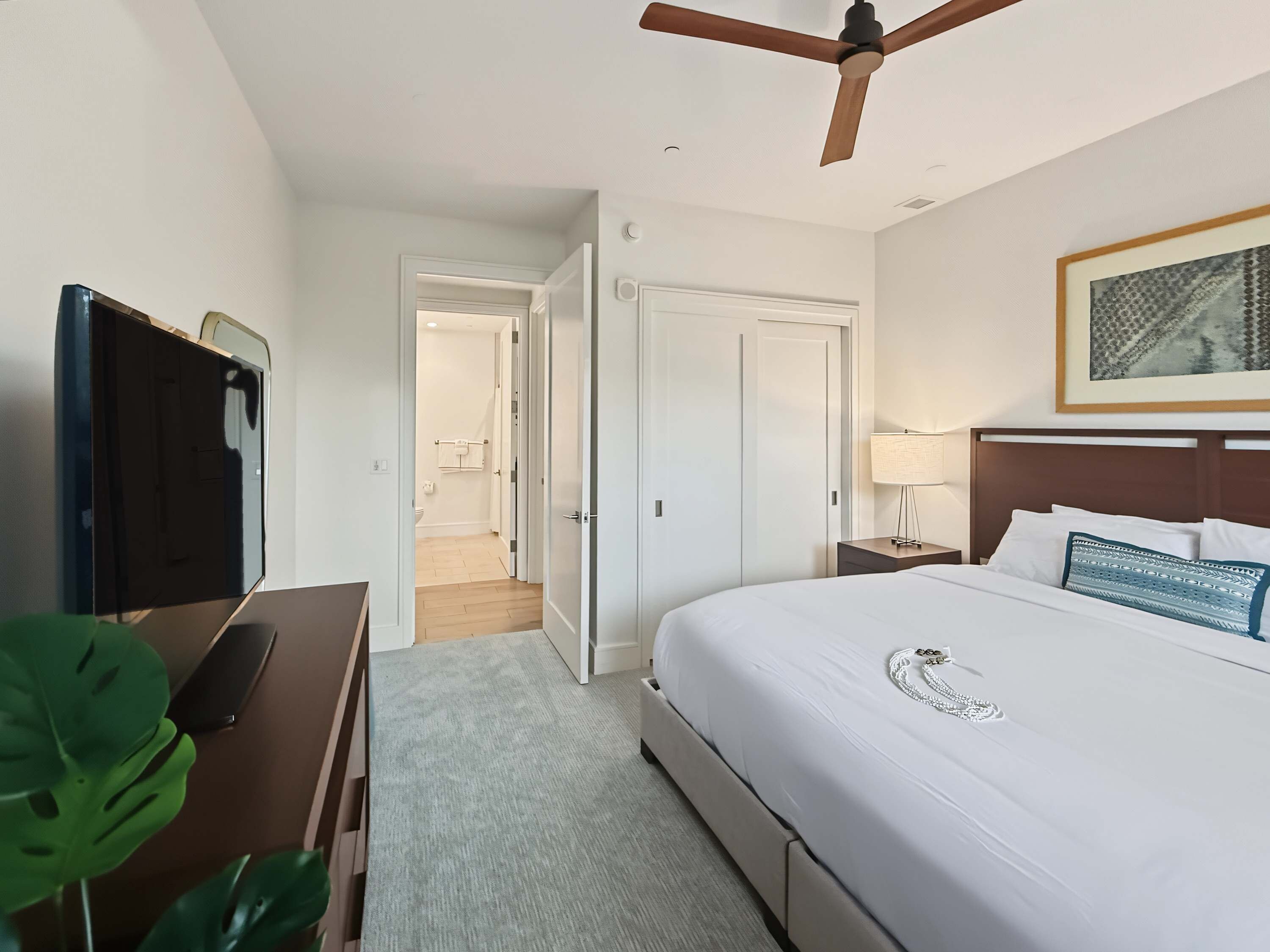 Una habitación de hotel con cama, mesita de noche, lámpara, ventilador de techo y televisor.