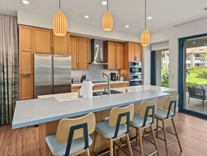 A modern kitchen with a central island, wooden cabinets, stainless steel appliances, and pendant lighting. - Spacious Ground-Level Villa Near Pool, Beachfront Resort Amenities (Lahaina)