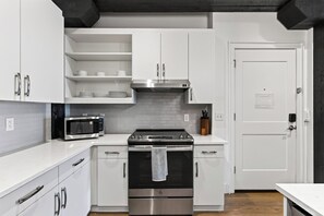 Una cuina moderna amb armaris blancs, un forn d'acer inoxidable, un microones i una campana extractora negra.