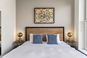 Ein Hotelzimmer mit einem großen Bett, zwei Nachttischlampen, einem hölzernen Kopfteil und einem Kunstwerk über dem Bett.