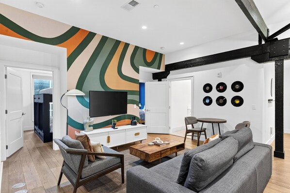 Ein modernes Wohnzimmer mit Fernseher, Couchtisch und Sofa. Schallplatten sind an der Wand angebracht, und eine Treppe führt in einen anderen Raum.