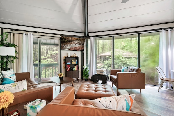 Ein geräumiges Wohnzimmer mit großem Fenster, Ledersofas, einem kleinen Tisch und einem Bücherregal.