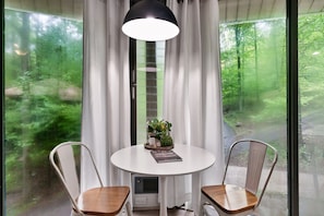 Ein Zimmer mit einem runden Tisch, zwei Stühlen, einer Topfpflanze und einem Buch.