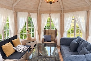 A room with a glass coffee table, a sofa, a chair, and large windows with curtains.