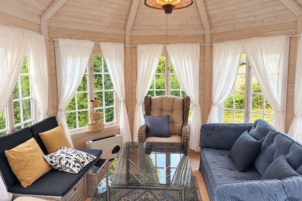 A room with a glass coffee table, a sofa, a chair, and large windows with curtains.