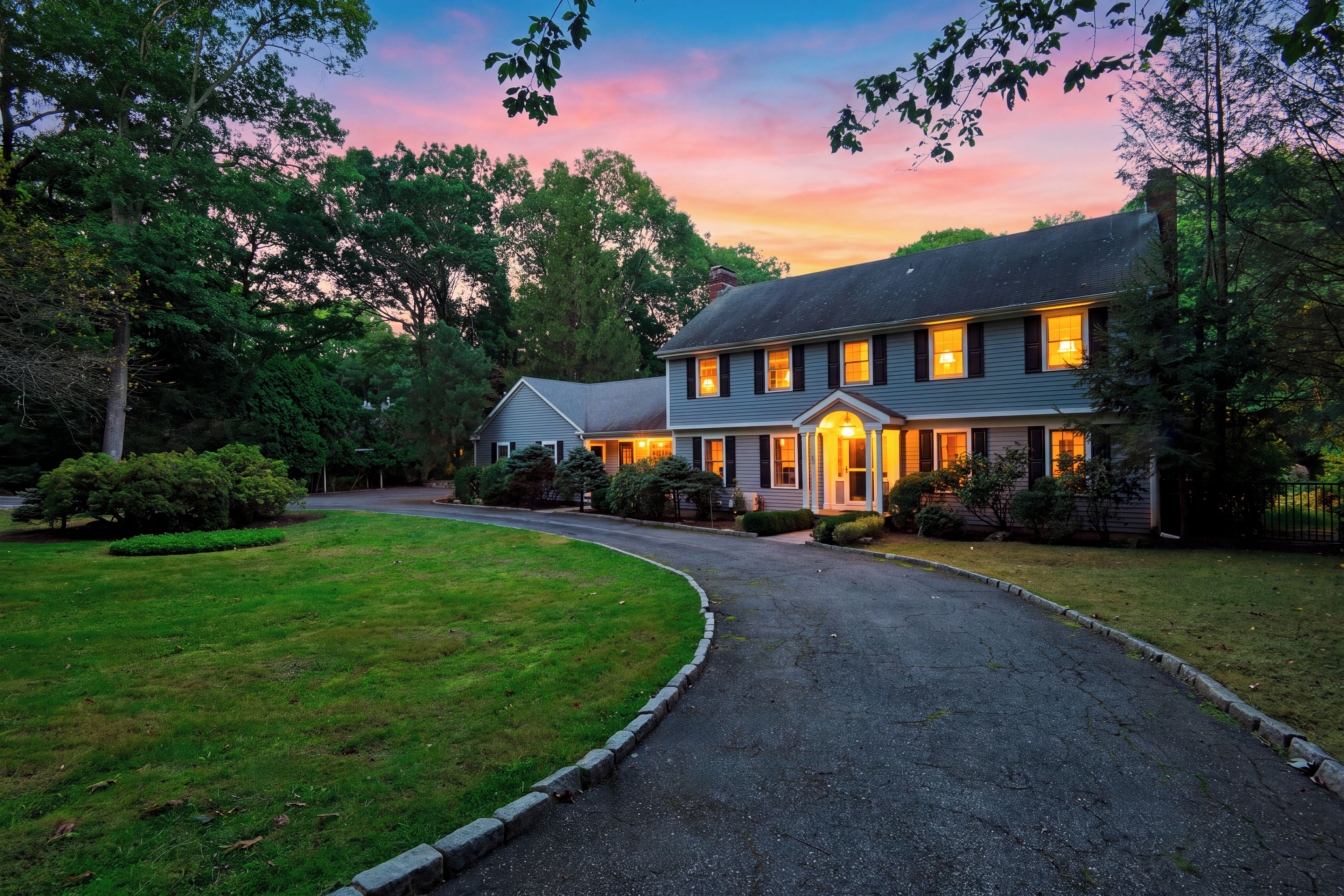 A two-story house with a driveway leading to the entrance, surrounded by greenery.