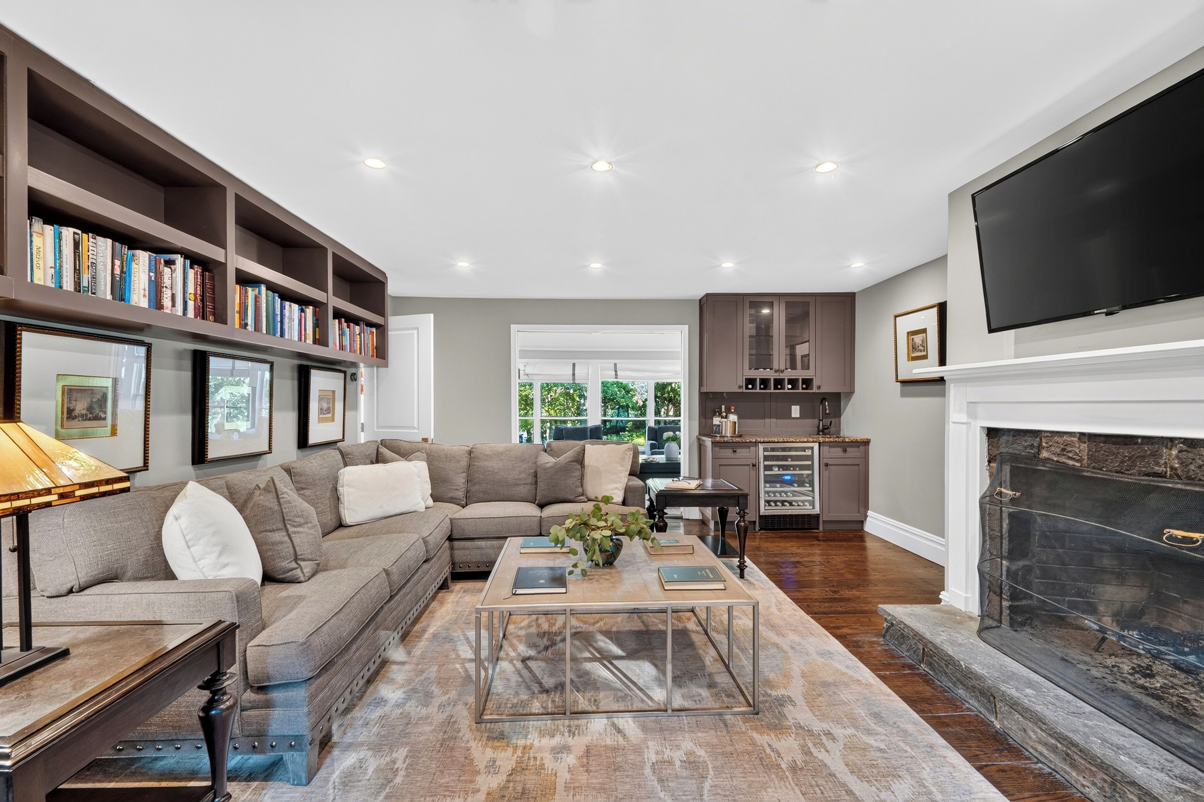 A living room with a sectional sofa, a coffee table, a bookshelf, a fireplace, and a kitchen area.