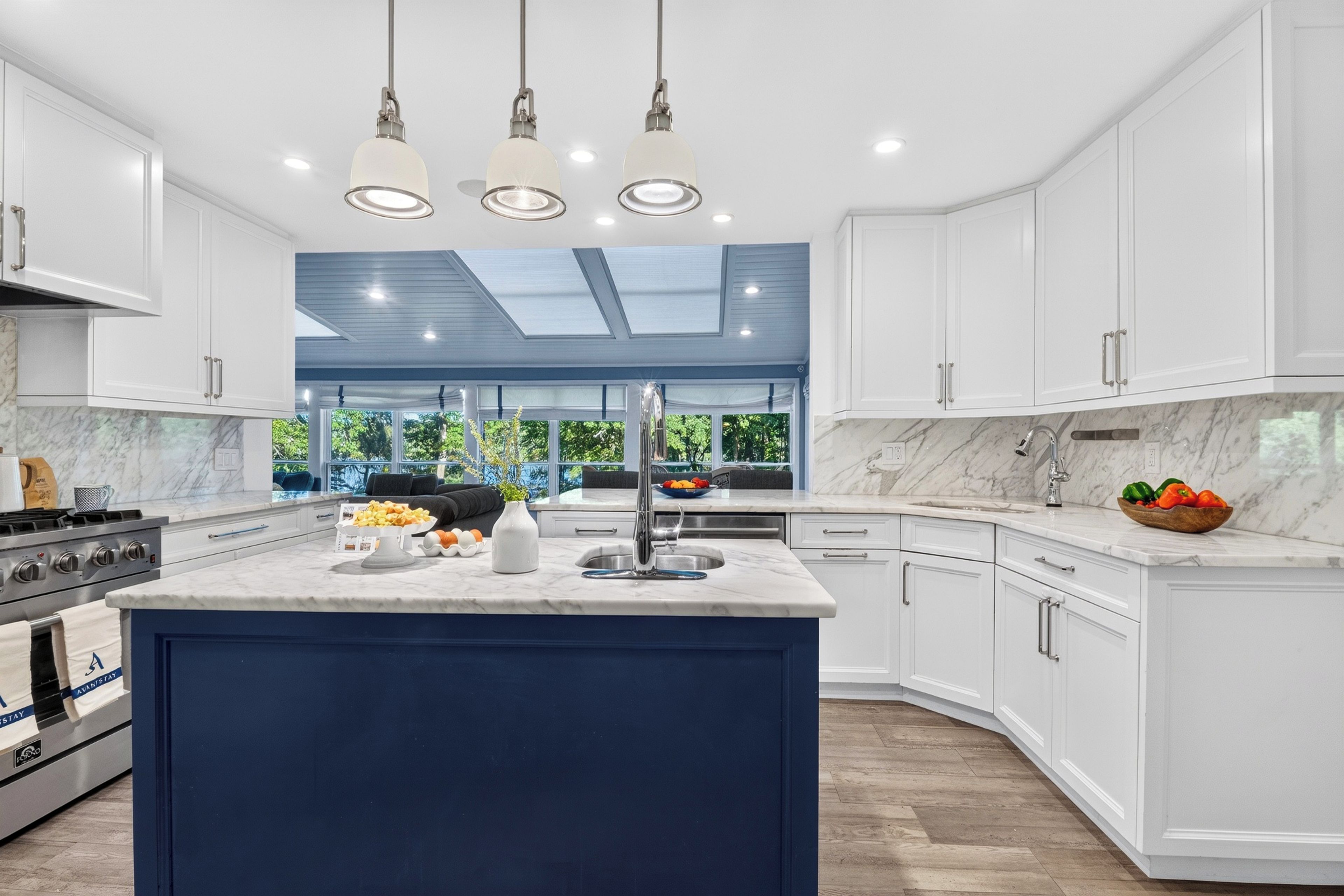 A modern kitchen with white cabinetry, a blue island, and a skylight.