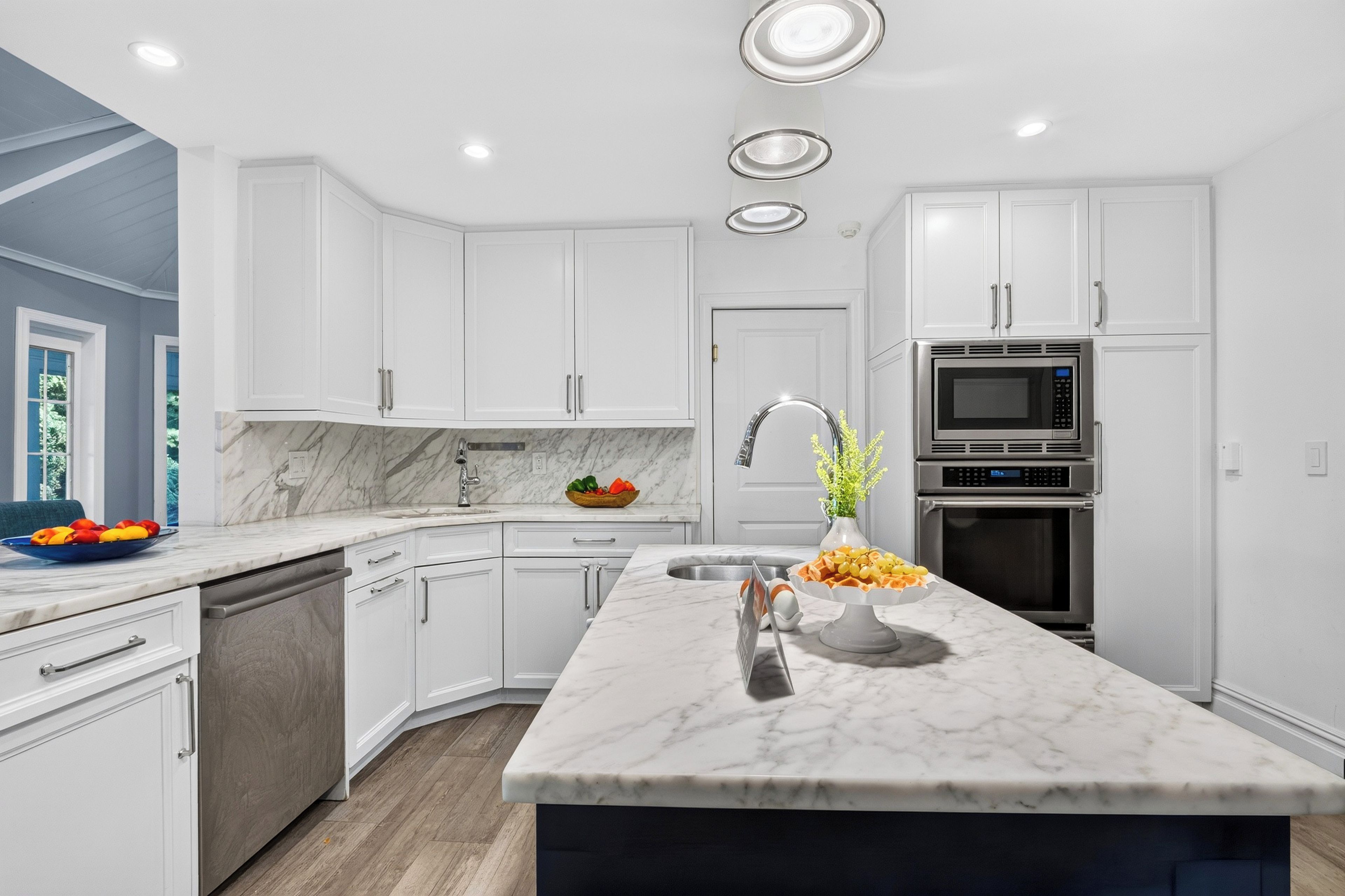 A modern kitchen with white cabinetry, a marble countertop, and stainless steel appliances.