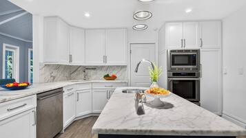 A modern kitchen with white cabinetry, a marble countertop, and stainless steel appliances.
