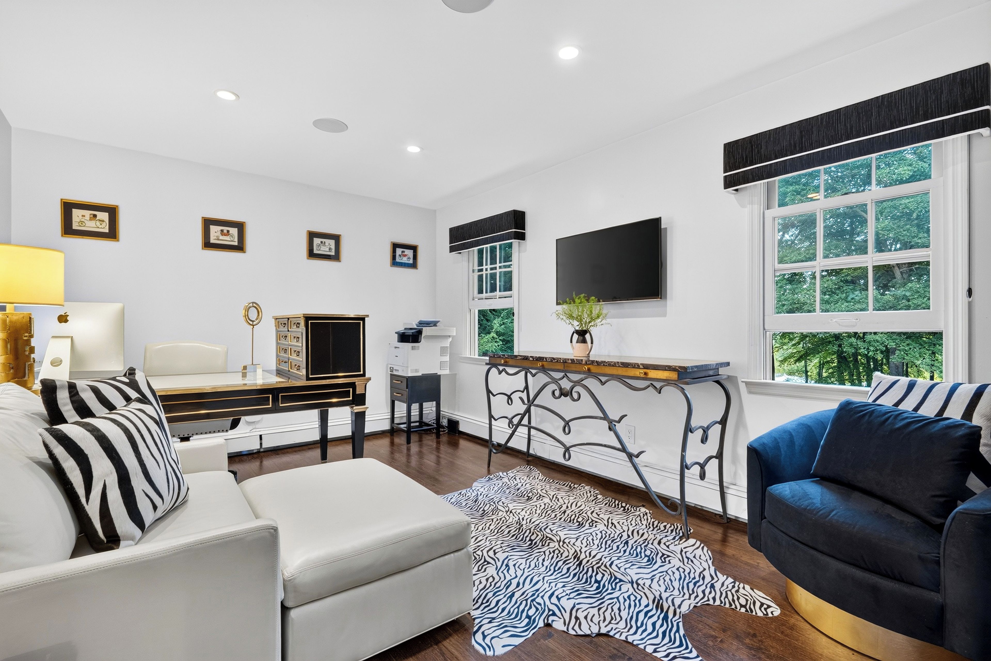 A modern living room with a sofa, a coffee table, a TV mounted on the wall, and a window with a view of trees.