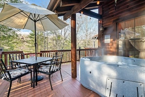 Eine Holzterrasse mit Whirlpool, Tisch und Stühlen sowie einem großen Sonnenschirm.