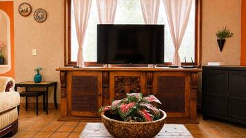Una sala de estar con televisor, un mueble de madera, un tazón decorativo grande y una ventana con cortinas.