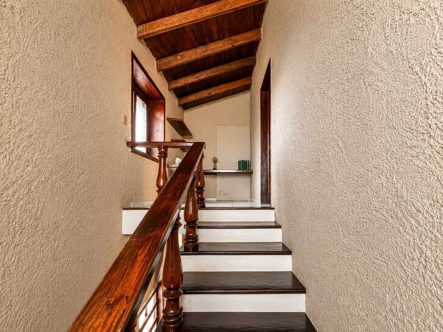 Un escalier avec des balustrades en bois et une main courante, menant à un palier avec un mur blanc et une étagère remplie de livres.