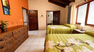 Una habitación con dos camas, un aparador de madera, un cuadro y una ventana con cortinas.