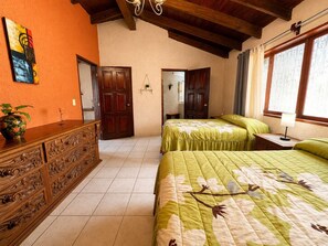 Una stanza con due letti, un comò in legno, un quadro e una finestra con tende.
