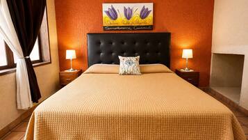 Habitación de hotel con una cama grande, dos mesitas de noche con lámparas, una chimenea y un cuadro floral en la pared.