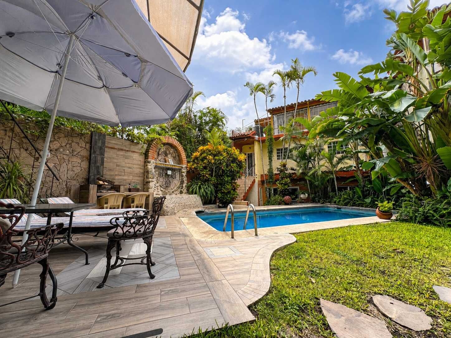 A pool area with a stone patio, a table with chairs, and a large umbrella.