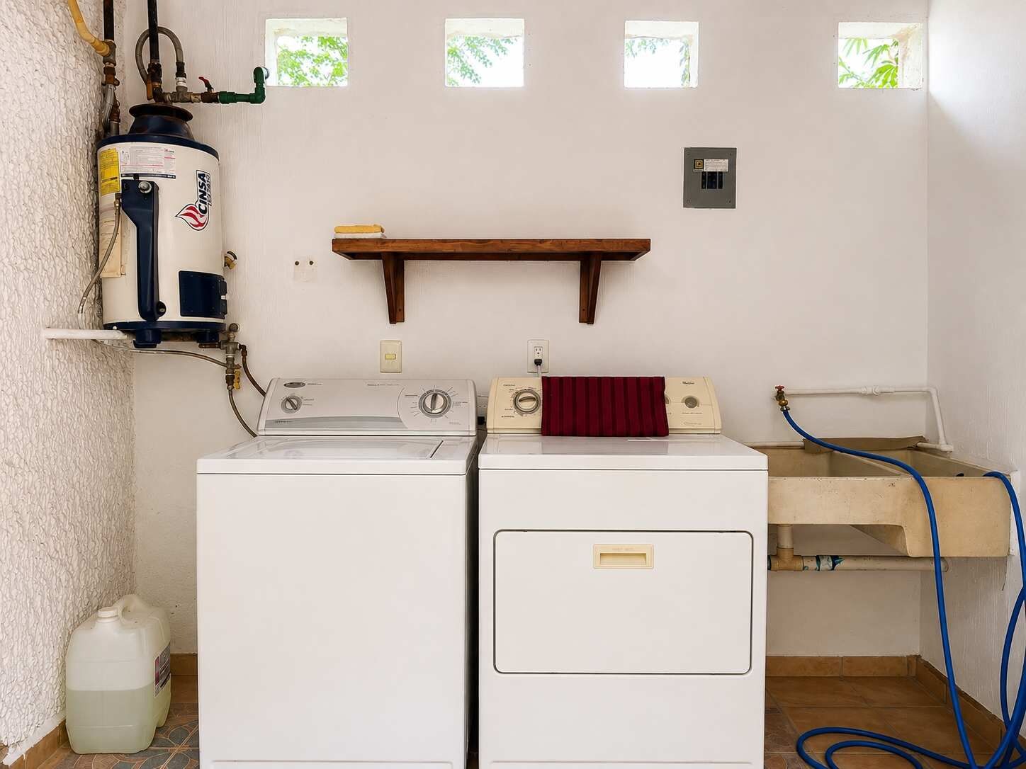 Een wasserette met twee witte wasmachines, een boiler en een houten plank boven de machines.