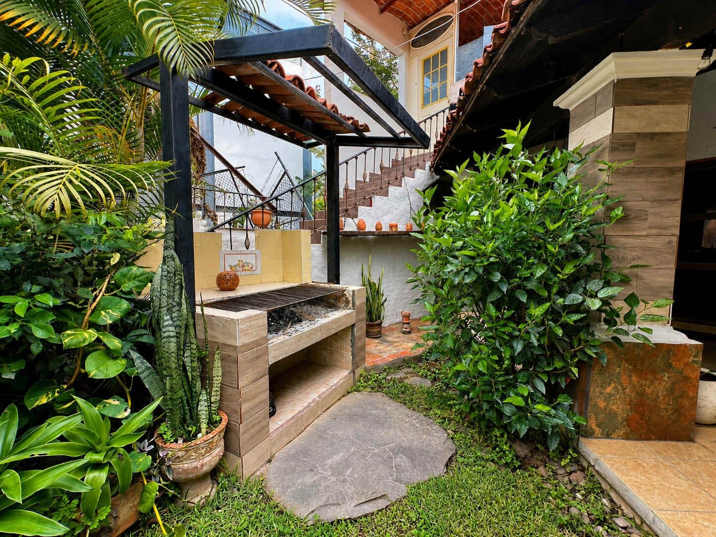 A patio with a grill, potted plants, and a staircase leading to a second floor.