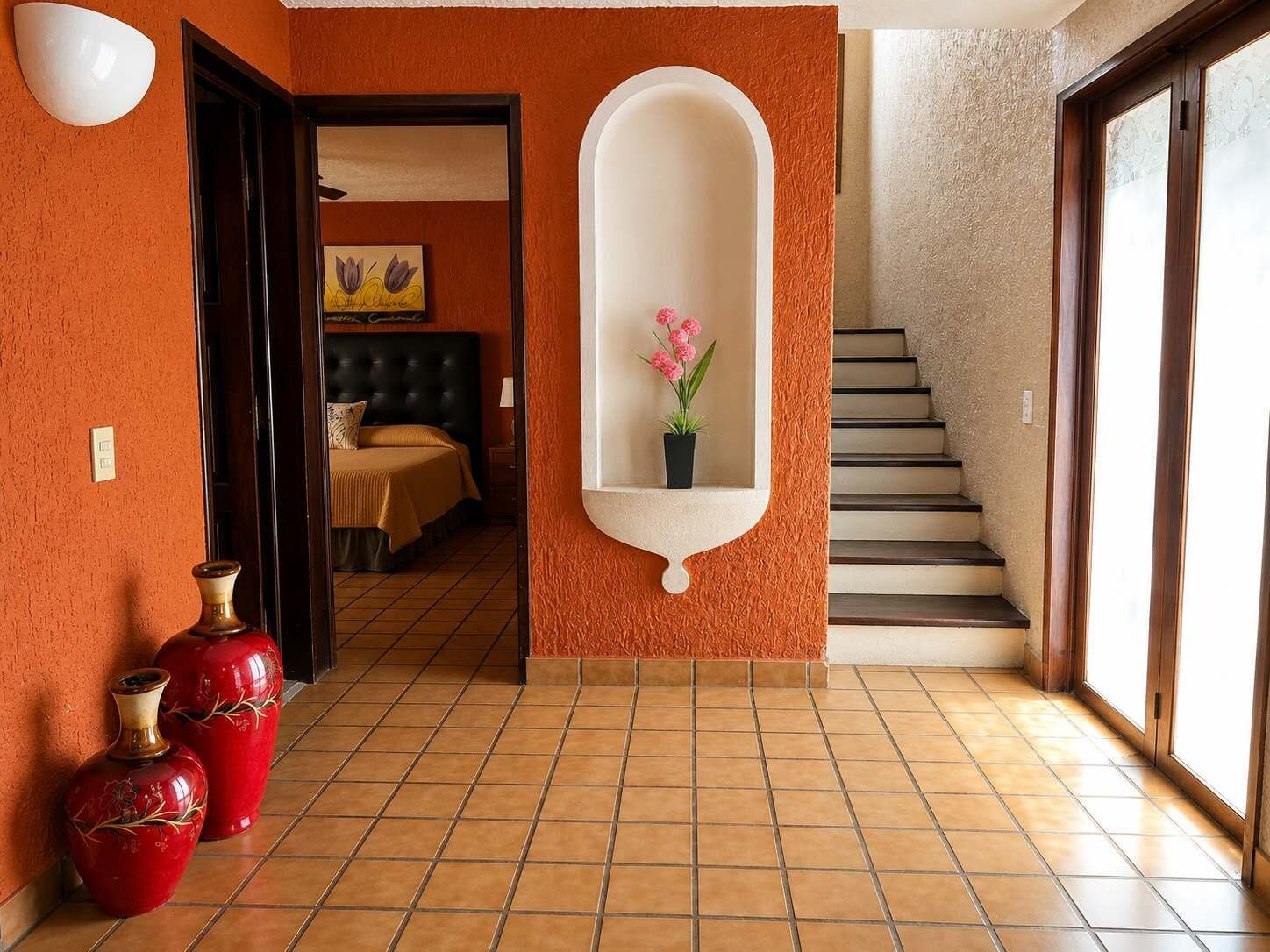 Un couloir doté d’un sol carrelé, d’un miroir fixé au mur et d’un escalier menant à une autre pièce.