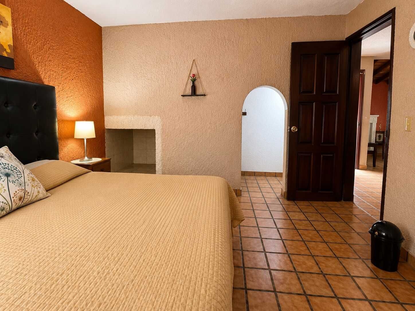 Une chambre d’hôtel comprenant un lit, une table de chevet, une lampe, une cheminée et une porte donnant sur une autre pièce.