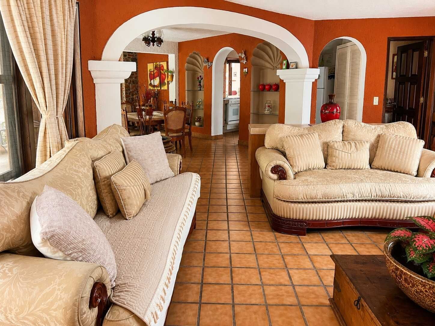 A living room with two sofas, a dining area, and a kitchen visible through an archway.