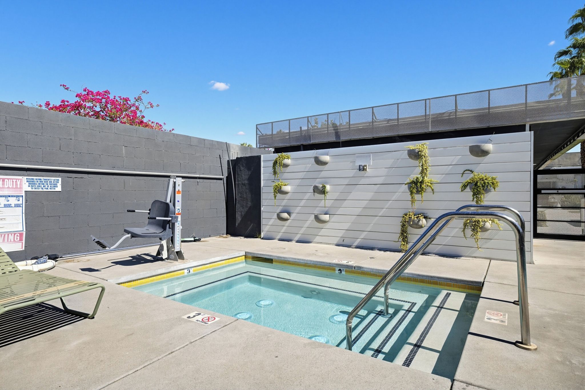 An outdoor swimming pool with a metal ladder, a bench, and a wall with planters.