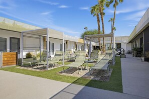 A modern outdoor lounge area with multiple seating options, including lounge chairs and benches, under a covered structure.