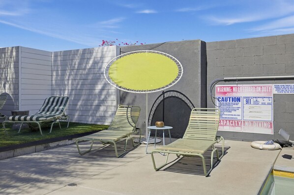 A pool area with lounge chairs, a yellow circular pool, and safety signs.