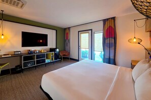 A hotel room with a large bed, a desk with a flat-screen TV, a chair, a small cabinet, and a window with curtains. - Semi-Private Patio Facing Pool + Firepit | Mtn Views | Garden King at Mahala (Palm Springs)