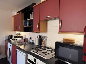 A compact kitchen with a gas stove, a microwave, and a washing machine. - A&R Guest House - 2-Bed Coach House, Bristol (Bradley Stoke)