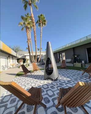 A sunny courtyard moment with a sculptural firepit, patterned tile, and lush desert landscaping. - Pool + Spa + Firepit + Courtyard | Mtn Views | Desert King at Mahala (Palm Springs)
