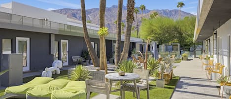 A modern outdoor seating area with green bean bags and tables, surrounded by palm trees and a mountain view.