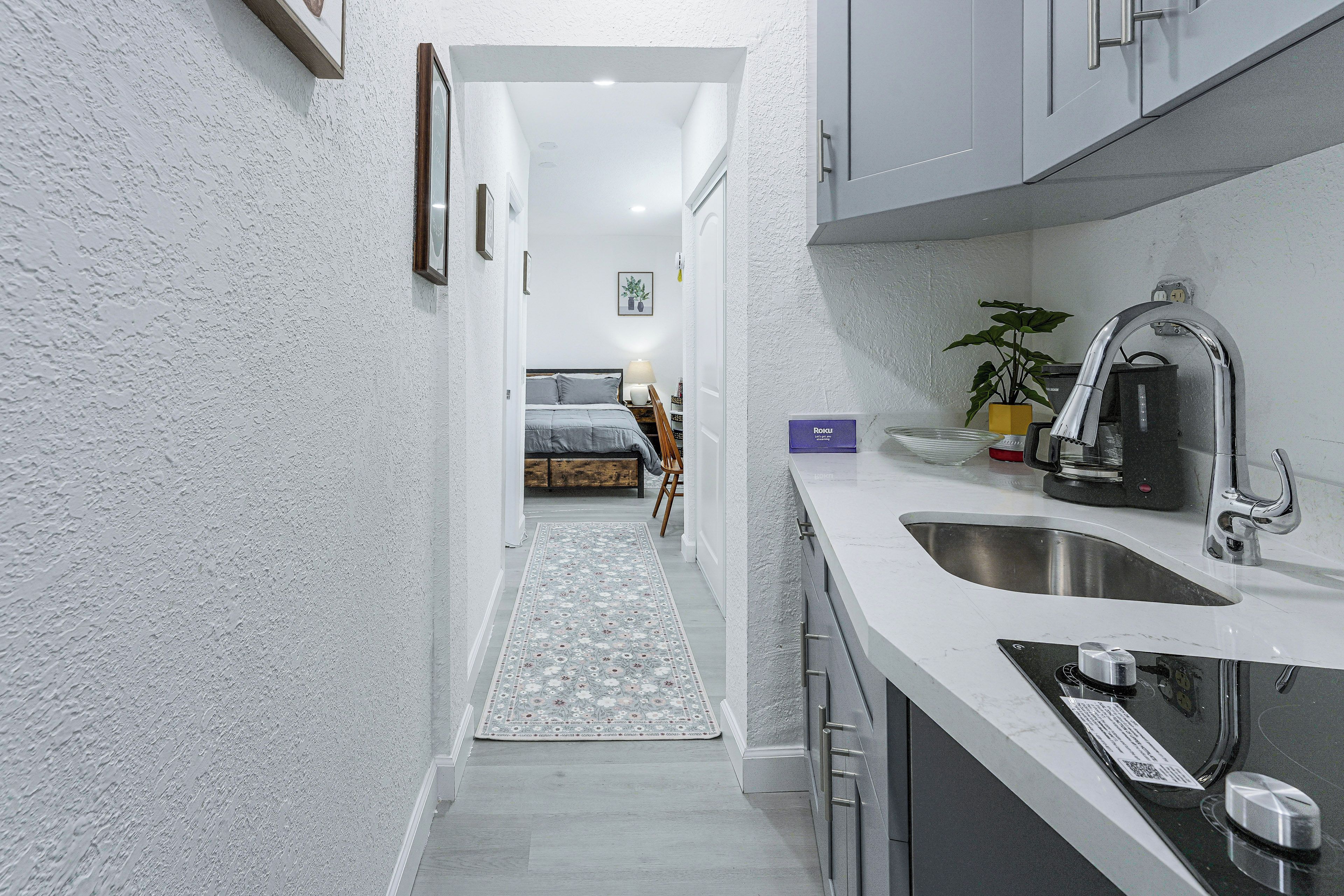 A narrow hallway leading to a bedroom with a bed, a bedside table, and a lamp.