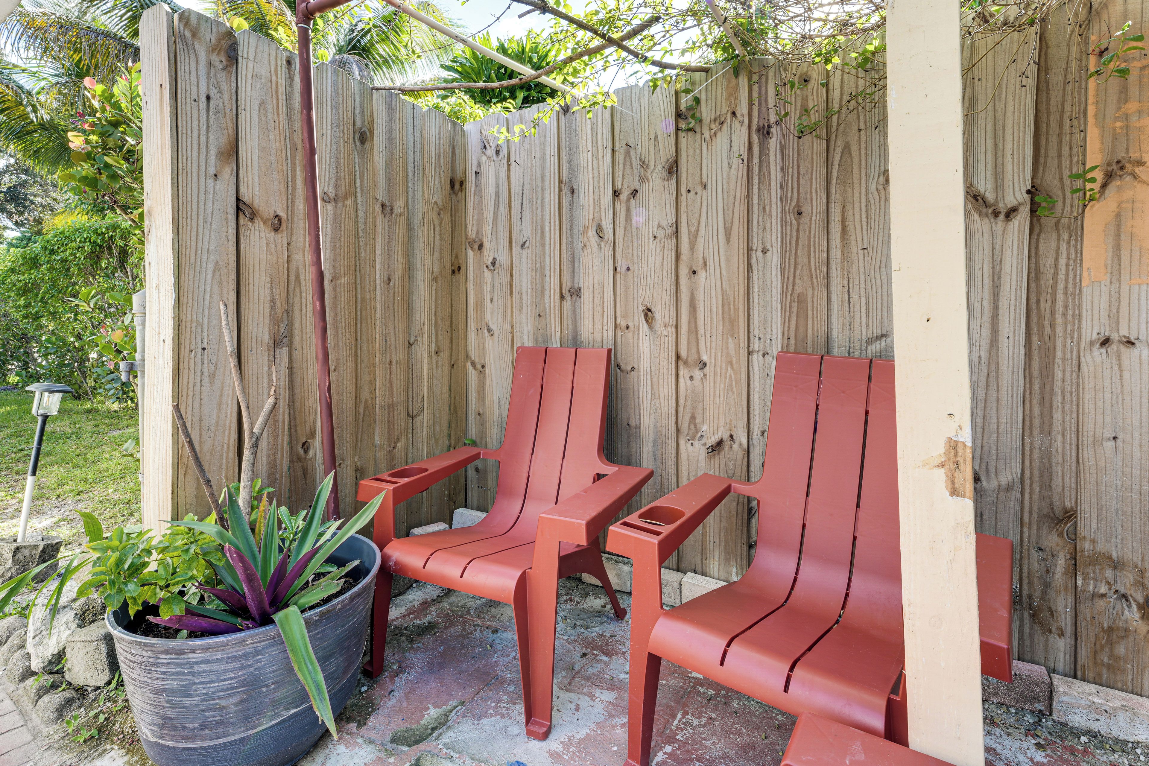 A wooden fence with two red plastic chairs and a potted plant.