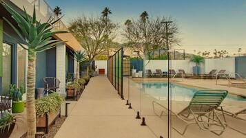 A poolside area with lounge chairs, a pool, and a pathway lined with plants and a chair.