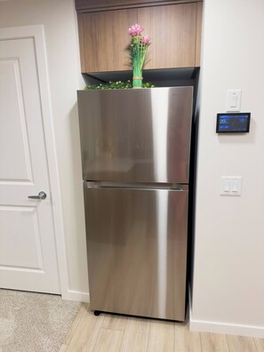 A stainless steel refrigerator with a digital display, a wooden cabinet above it, and a white door to the left. - Private Suite Near Calgary Airport (Calgary)