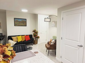 A living room with a black sofa, a brown chair, a small table, and a door. - Private Suite Near Calgary Airport (Calgary)