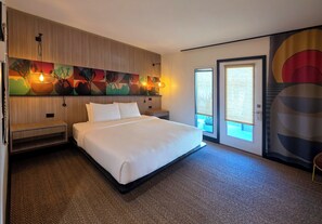 Habitación de hotel con una cama grande, cabecera de madera, una obra de arte en la pared y una puerta que da a un balcón.