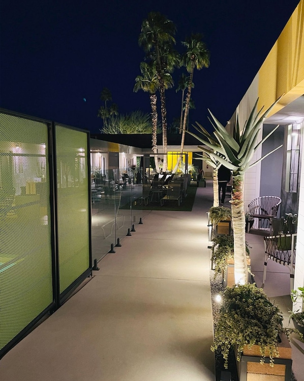 Glowing evening pathways, palms, and colorful architecture create a welcoming resort atmosphere. - Pool + Spa + Firepit + Courtyard | Mtn Views | Desert King at Mahala (Palm Springs)