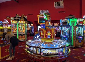A brightly lit arcade with various gaming machines, including a prominent Minion-themed game.