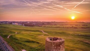 A grassy field with a circular structure in the foreground and a sunset in the background.