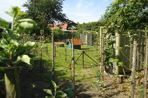 Un jardín con una valla de madera, una pequeña estructura verde y una casa con techo rojo al fondo.