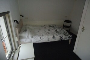 A small, single-bed room with a white bedspread and a black chair. - Holiday apartment with 3 bedrooms (Vrouwenpolder)