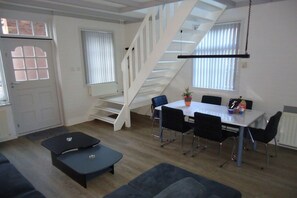 A modern living space with a staircase, a dining area with chairs and a table, and a sofa. - Holiday apartment with 3 bedrooms (Vrouwenpolder)