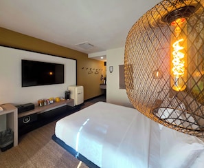 A hotel room with a bed, a TV mounted on the wall, a small refrigerator, and a decorative light fixture. - Pool + Spa + Firepit + Courtyard | Mtn Views | Sun Queen at Mahala (Palm Springs)
