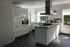A modern kitchen with white cabinetry, a central island, and a large window providing natural light. - Palace by the Sea Joossesweg (Westkapelle)