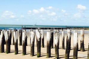 A sandy beach with wooden posts and a sailboat in the distance. - Palace by the Sea Joossesweg (Westkapelle)